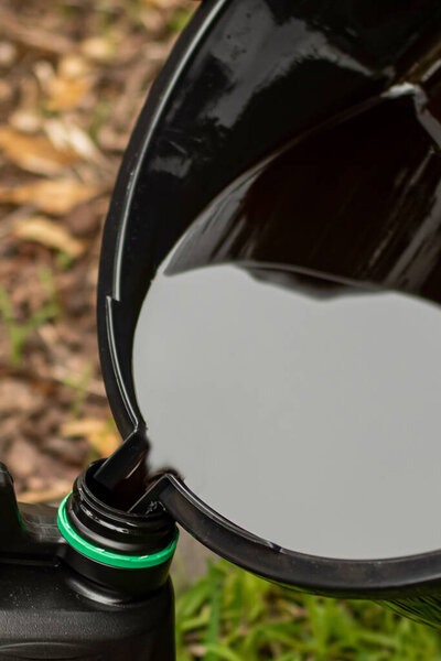 Transfering of used drained motor oil from the black tray to the empty container. DIY change engine motor oil Disposing of old oil