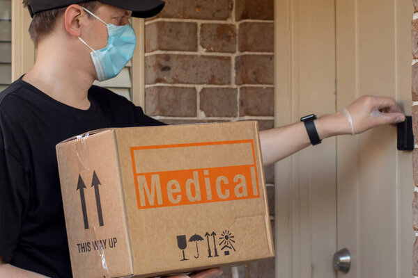 Contactless delivery during COVID-19 pandemic lockdown concept. Courier wearing mask and gloves holds a parcel with medical equipment and knocks on the door.