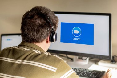 Sydney, Avustralya - 2020-04-06 Erkek woth kulaklıkları zoom bulut toplantılarının logosuna bakan bir monitöre bakıyor. Coronavirus ev konseptinden kilitlenme çalışması