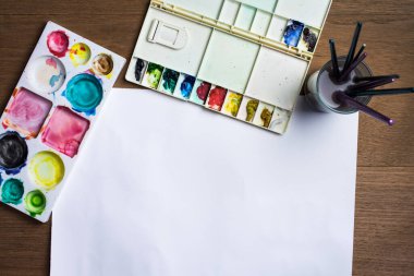 Ahşap arka planda renkli suluboya ve teçhizatlı beyaz kağıt.