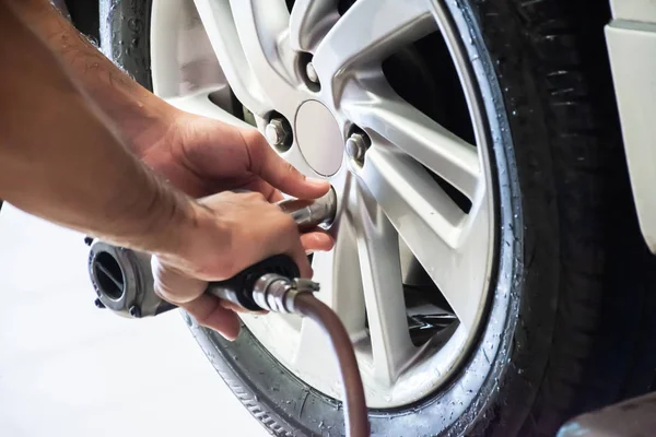 Professional car mechanic using an electric screwdriver to loosen the bolts for changing car wheel in auto repair and service shop. — 스톡 사진