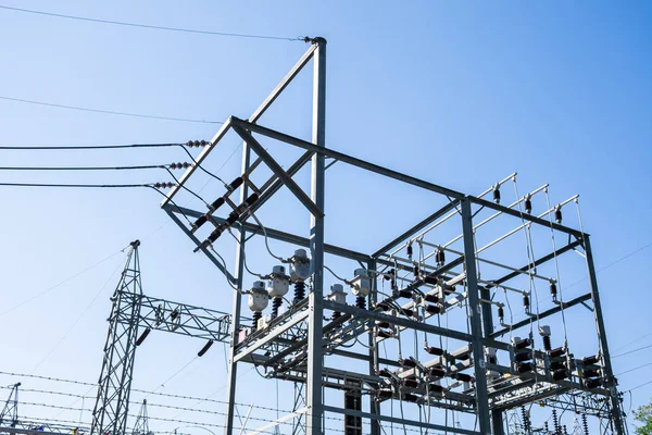 Pólos elétricos de aço e linhas na central elétrica de alta tensão contra o sol e o céu azul claro . — Fotografia de Stock