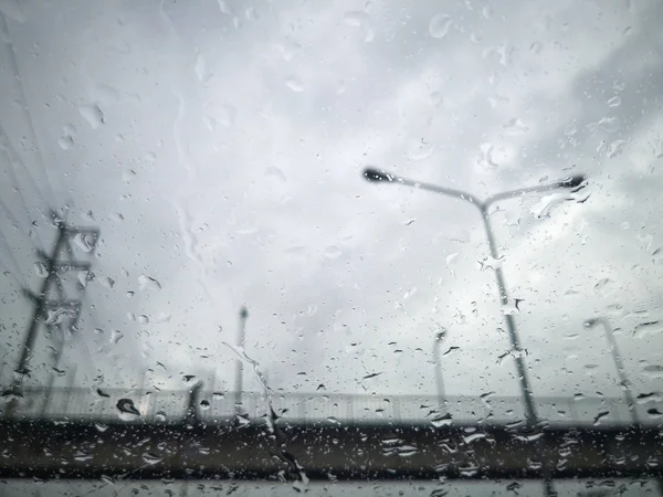 Regen druppels op het autoruit met voetgangersbrug en elektrische pool wazig achtergrond. — Stockfoto