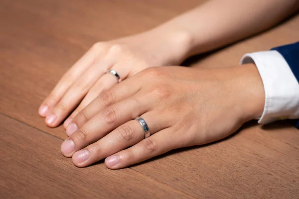 Bruid en bruidegom hand in hand met trouwring op houten tafel. — Stockfoto