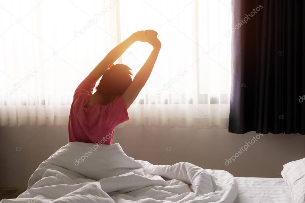 Asian woman waking up and stretching relax in sunny day morning. Happy rest day concept.