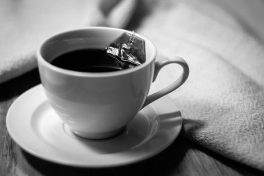 Çay poşeti ve sıcak suya batırılmış çay, ahşap ve pamuk kumaş arka planda..