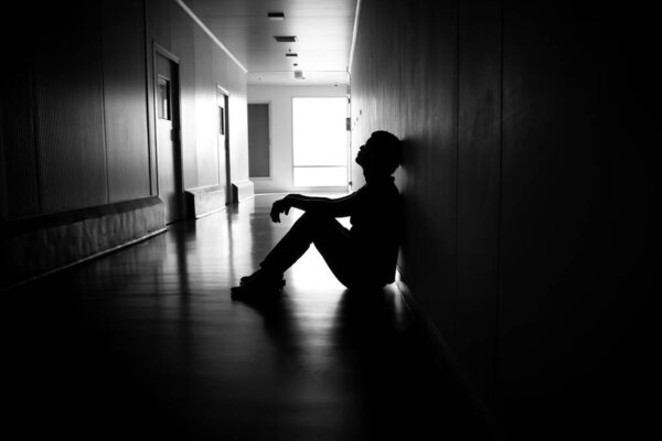 Silhouette of depressed man sitting on walkway of residence building. Sad man, Cry, drama, lonely and unhappy concept.