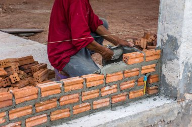 İnşaat işçisi dış duvarlar için çimentoya tuğla yerleştiriyor..