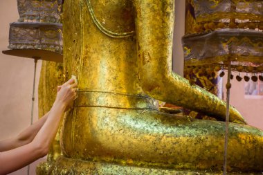 İnsanlar, tapınakta altın yapraklı Buda heykelini örterler. Tayland geleneğidir..