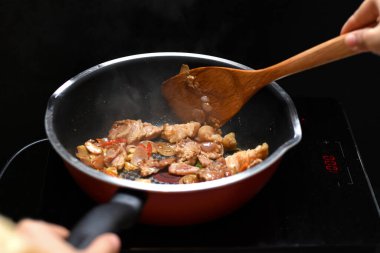 Kızarmış domuz eti ve kırmızı soğanı karıştırmadan önce sebzeyi tencere tavasının ısı kaynağına koy..