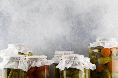 Mavi arka planda cam bir kavanozda salatalık ve domates turşusu.