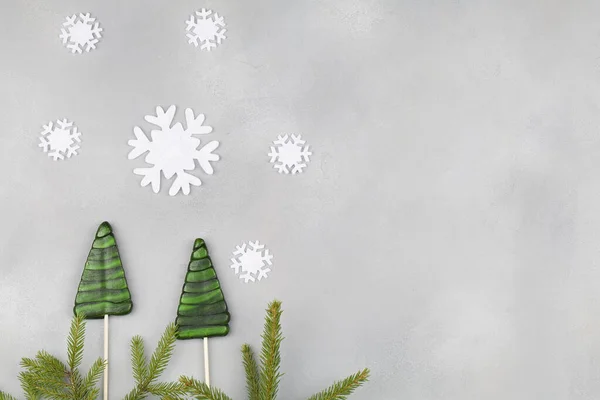 Зеленые леденцы в форме рождественской елки с ветвями елки и белыми снежинками на голубом фоне . — стоковое фото