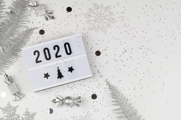 Figuren 2020 op lichtbak met witte sneeuwvlokken, zilveren takken en decoraties op witte achtergrond — Stockfoto