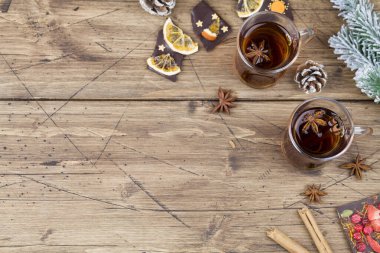 Tarçınlı sıcak çay, anason, meyveli çikolata, kozalak ve ağaç dallı ahşap zemin üzerinde noel ağacı.