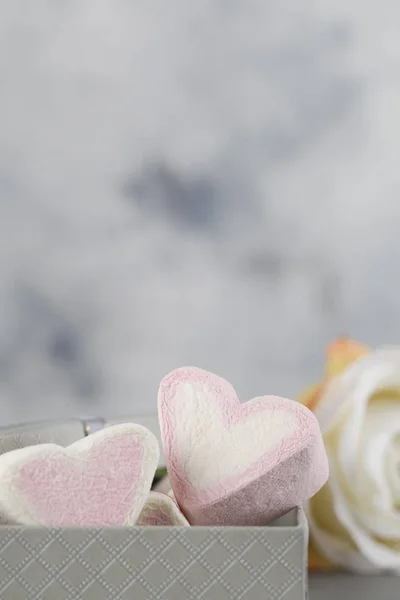 Hvid og lyserød slik i form af hjerter i kasse på grå baggrund med blomst. Valentines dag minimalisme baggrund . - Stock-foto