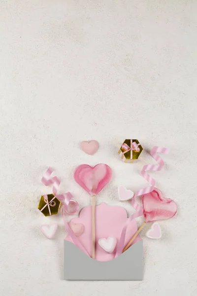 Caramelo blanco y rosa en forma de corazones, lollipops rosa cinta, regalos en sobre sobre fondo blanco . — Foto de Stock