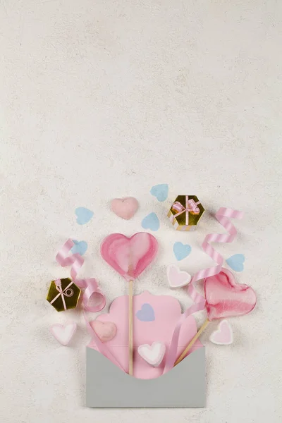 Caramelo blanco y rosa en forma de corazones, lollipops rosa cinta, regalos en sobre sobre fondo blanco . — Foto de Stock