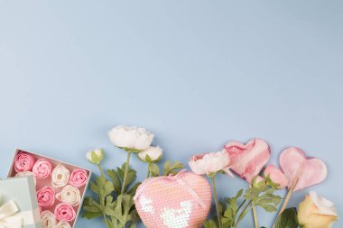 Kutuda güller şeklinde beyaz ve pembe şekerler, çiçekler, dekorasyon, hediyeler ve mavi arka planda lolipoplar..