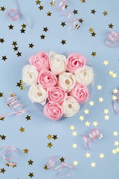 White and pink candy in form of roses in box , pink ribbon and small stars on blue background. — 스톡 사진