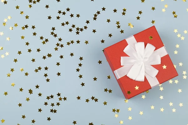 Červená dárková krabice s bílou stuhou na modrém pozadí s malými hvězdami. — Stock fotografie
