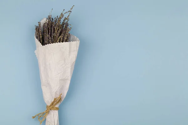 Bouquet of dry lavender flowers in craft white paper on blue background. — Stock Photo, Image
