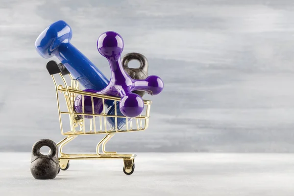 Blue dumbbell, massager in shopping cart on blue wooden background. — Stock Photo, Image