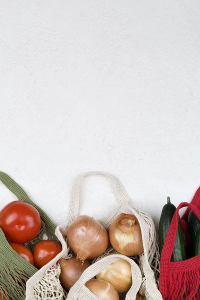 Bolsa de compras de malla blanca, verde y roja con tomates rojos, lazo y pepinos verdes sobre fondo blanco . — Foto de Stock