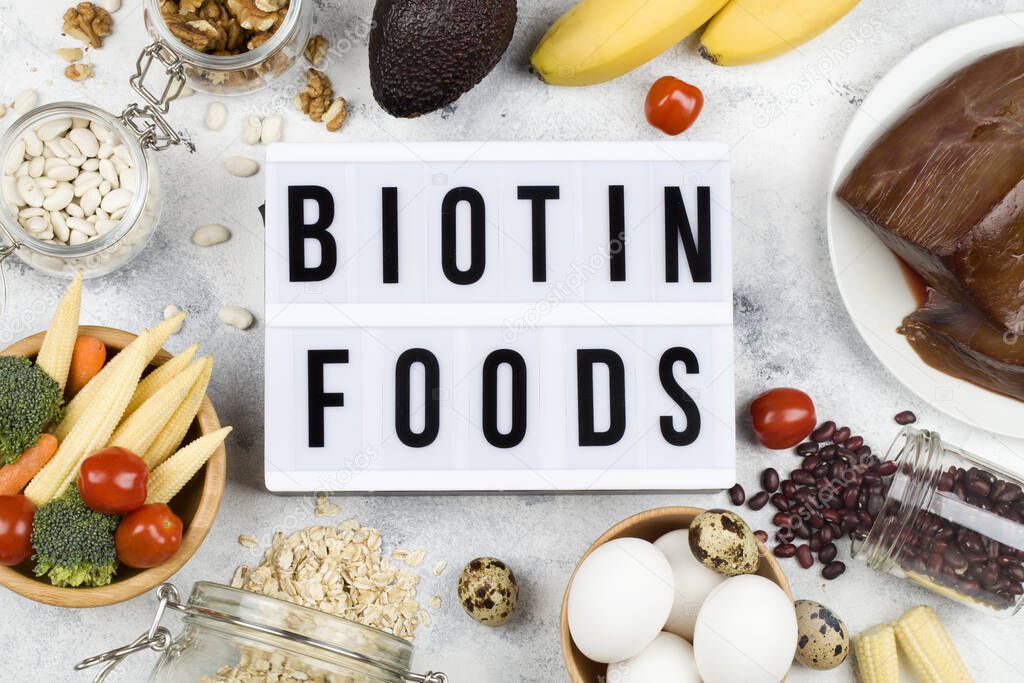 Food rich in biotin. food : tomato eggs walnuts beans corn avocado broccoli carrot liver oatmeal bananas on blue background with light box inscription biotin foods , natural food top view flat lay