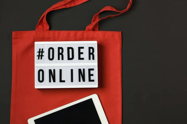 lightbox with words order online. Online shopping concept. Laptop with red cotton shopping bag on black background. Top view, flat lay, copy space. Zero waste, eco friendly , coronavirus concept