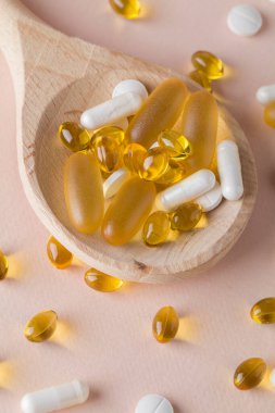 Doğal vitaminler ve pembe arka planda tahta kaşıklarda takviyeler. Üst görünüm düzlüğü dikey olarak yatar