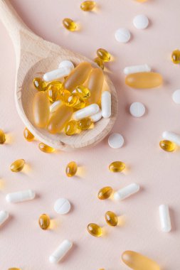 Doğal vitaminler ve pembe arka planda tahta kaşıklarda takviyeler. Üst görünüm düzlüğü dikey olarak yatar