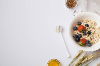 Çilekli yulaf lapası, yaban mersini, keten tohumu ve bal beyaz arka planda. Sağlıklı vejetaryen yemeği. Boşluğu kopyala