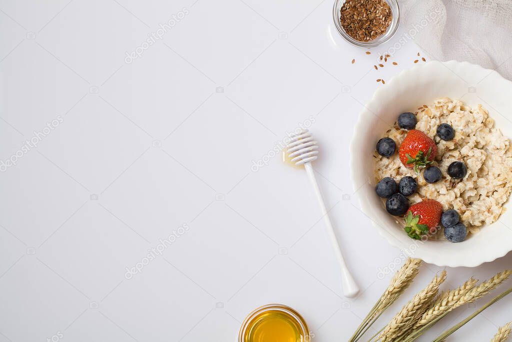 Oatmeal porridge with strawberry, blueberry, flax seeds and honey on white background. Healthy breakfast vegetarian food. copy space