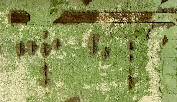 Paslı metal elementlerle kaplı, yeşil boya kalıntılarıyla kaplı eski bir beton duvarın arka planı. Eski duvarın dokusu, kapatın..