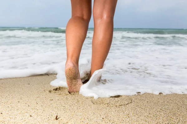 Fechar os pés descalços de um homem andando em uma praia, com uma onda e — Fotografia de Stock