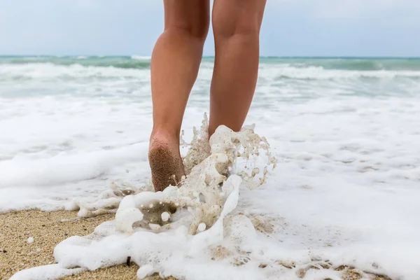 Fechar os pés descalços de um homem andando em uma praia, com uma onda e — Fotografia de Stock
