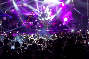 Parlak sahne ışıkları önünde konser kalabalığının siluetleri