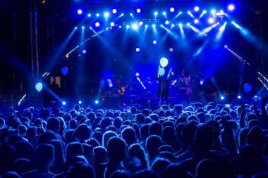 Parlak sahne ışıkları önünde konser kalabalığının siluetleri