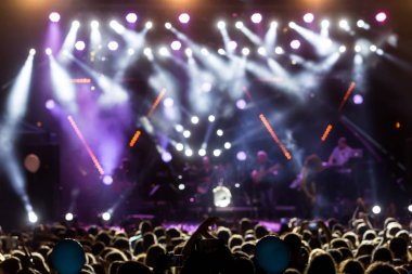 Parlak sahne ışıkları önünde konser kalabalığının siluetleri