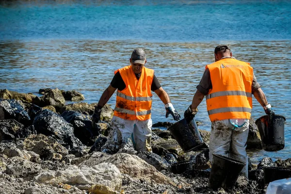 Los trabajadores tratan de limpiar el aceite que se ha arrastrado a tierra, en una playa o — Foto de Stock