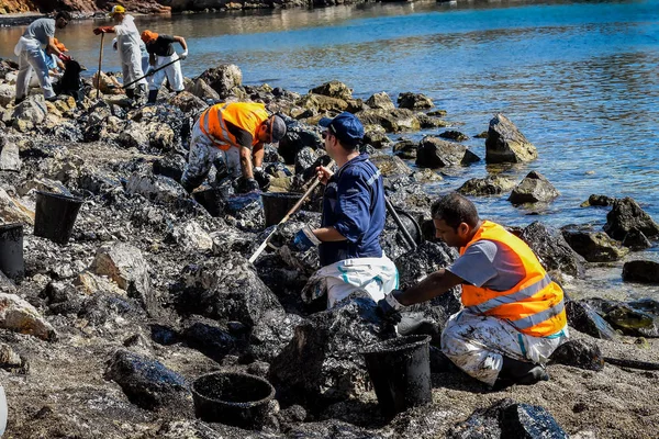 Los trabajadores tratan de limpiar el aceite que se ha arrastrado a tierra, en una playa o — Foto de Stock