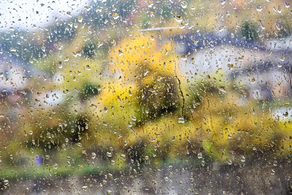 Gotas de lluvia en una ventana. Edificios borrosos y árboles en segundo plano — Foto de Stock