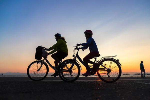 Silhouetten von Menschen, die einen Spaziergang mit dem Fahrrad an der Küste von — Stockfoto