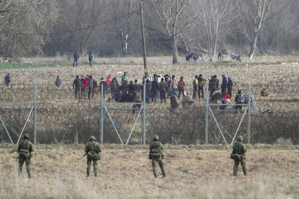 Kastanies, Evros, Greece - March 2, 2020: Greek police and soldiers in front of a fence trying to deter migrants as they attempt to enter Greece from Turkey at the Greek-Turkish border in Kastanies