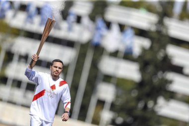 Athens, Greece - March 19, 2020: Olympic Flame handover ceremony for the Tokyo 2020 Summer Olympic Games. Greek Olympic medalist  E. Petrounias holds the Tokyo Olympic Flame at the Panathenaic stadium clipart