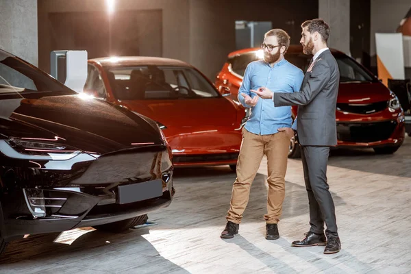 Cliente con un vendedor en la sala de exposición con coches eléctricos — Foto de Stock