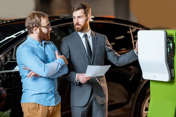 Cliente con un vendedor en la sala de exposición con cargos de coche — Foto de Stock