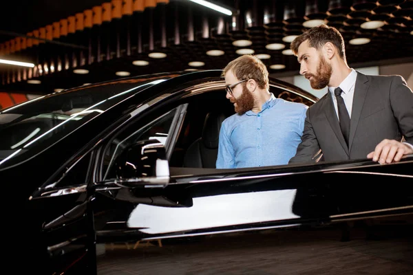 Cliente con un vendedor en la sala de exposición con coches eléctricos — Foto de Stock