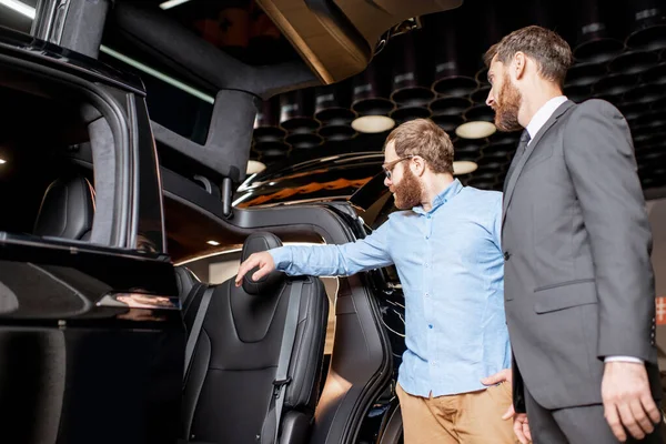 Kund med en försäljningschef inspekterar modern bil i showroom — Stockfoto