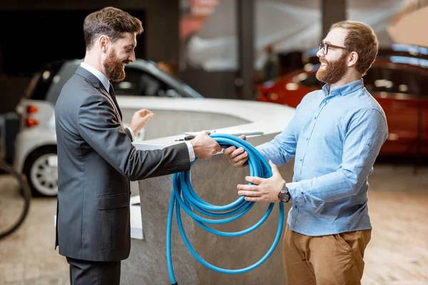 Salesman giving cable for electric car charging to a client